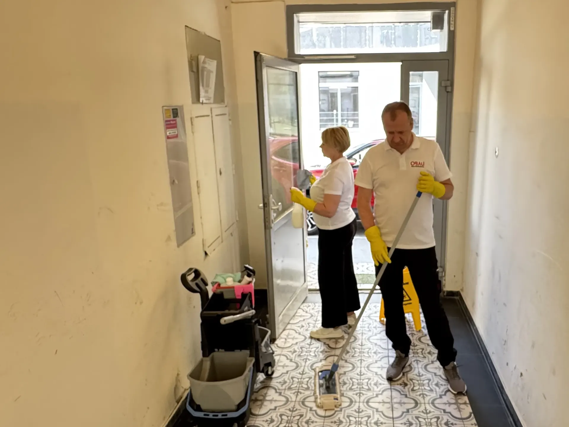 Zwei OBAU Mitarbeiter reinigen gleichzeitig die Glasschnittstelle und den Stiegenhausboden